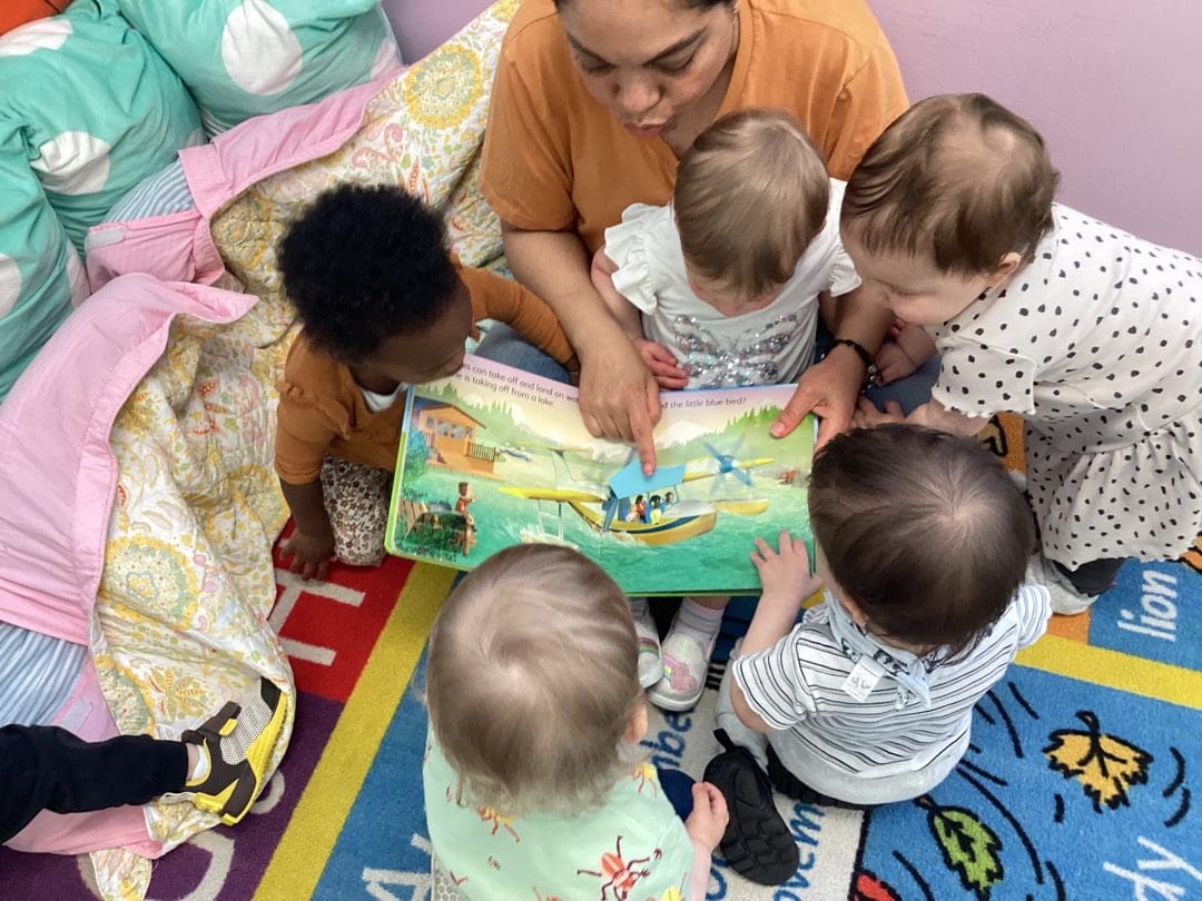 A group of babies are sitting around a book.