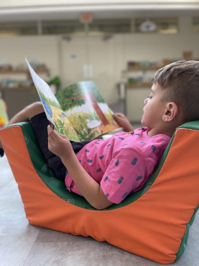 A little boy sitting in a chair reading a book.