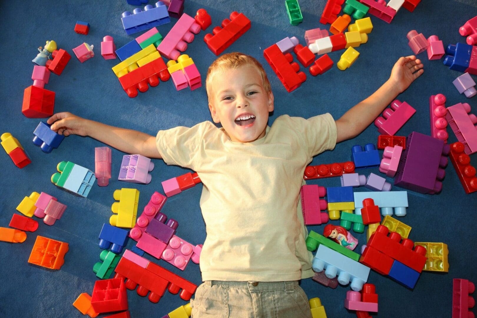 A boy laying on the ground with many colorful blocks.