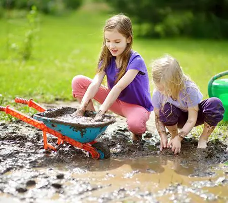 Two little girls playing in a puddle with a toy truck.
